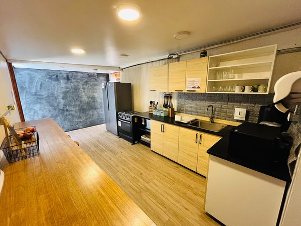 Cocina equipada con mesa larga de madera, nevera grande, horno y muebles claros